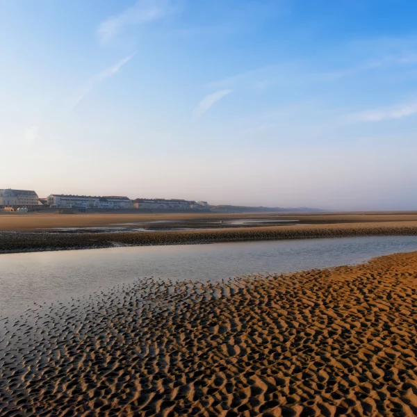 Plage tranquille avec ciel bleu et bâtiments au loin.