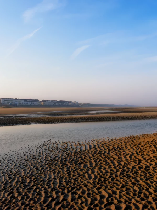 Plage tranquille avec ciel bleu et bâtiments au loin.
