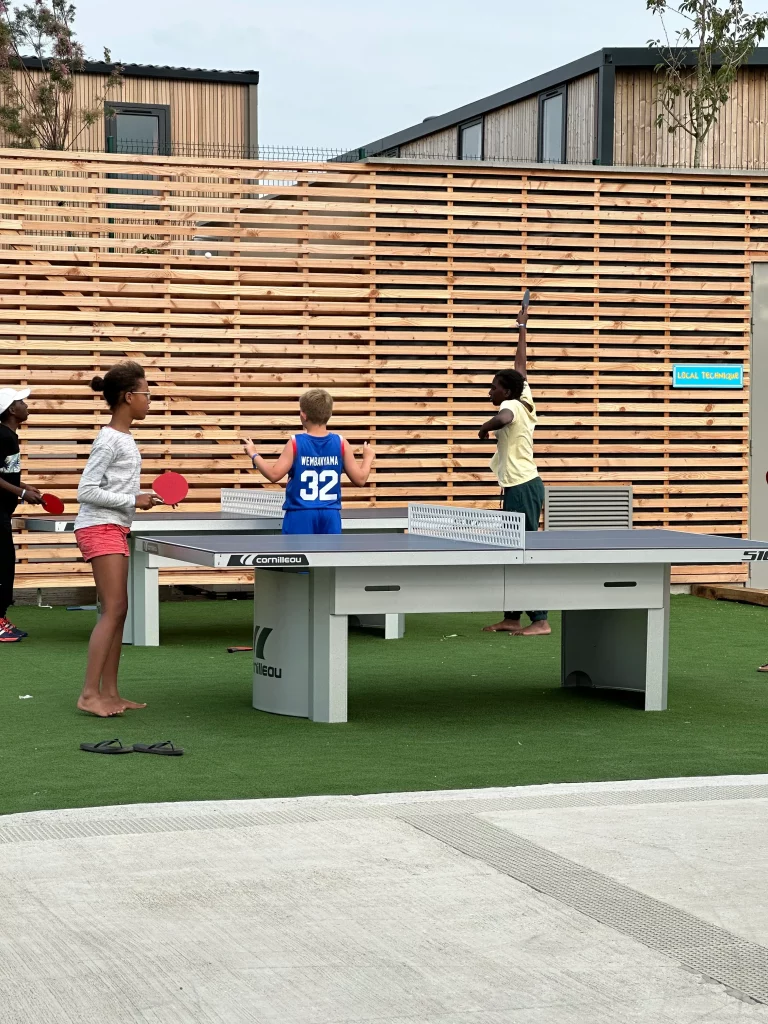 Enfants jouant au ping-pong en extérieur.