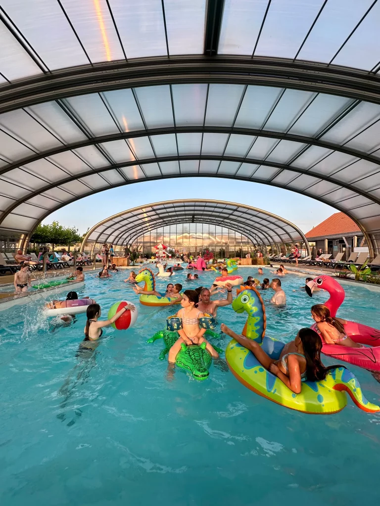 Piscine couverte avec enfants sur bouées colorées.