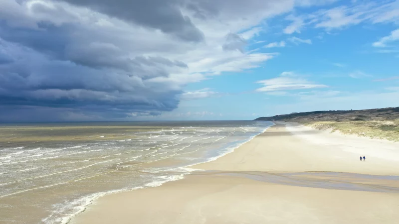 Plage sableuse, ciel nuageux et bleu.