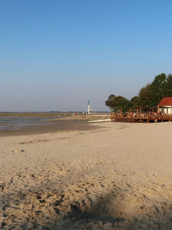 Plage avec chalet, dunes et phare.