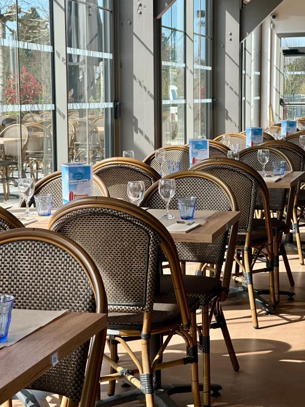Salle de restaurant ensoleillée, tables vides.