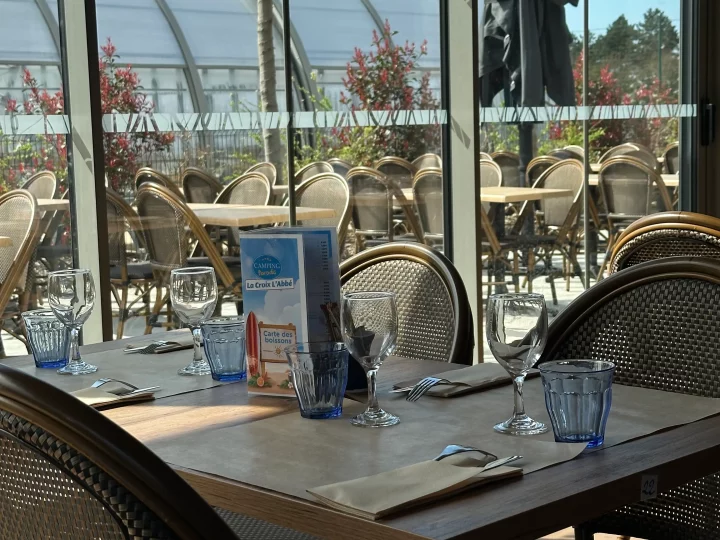 Table de restaurant avec verres et couverts, terrasse extérieure.